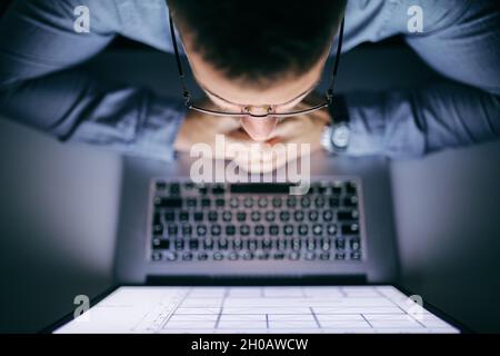 Draufsicht auf einen Geschäftsmann, der seinen Laptop ansah, während er spät in der Nacht im Büro saß. Stockfoto