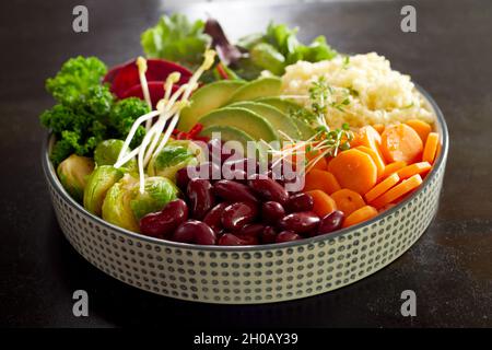 Eine große, schmackhafte Buddha-Schüssel mit Gemüse und Couscous, serviert auf einem schwarzen Tisch für ein gesundes vegetarisches Mittagessen Stockfoto