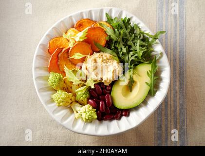 Draufsicht auf die Buddha-Schüssel mit appetitanregenden verschiedenen Gemüsesorten und Hummus, der für ein vegetarisches Mittagessen auf den Tisch gelegt wird Stockfoto