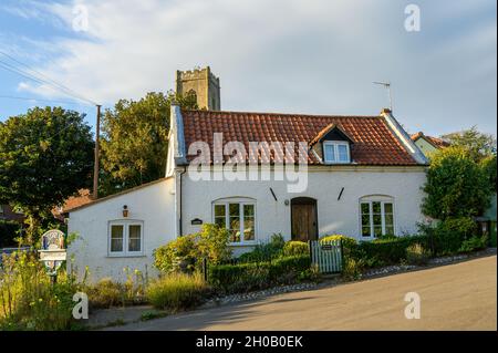 Camberley Cottage, ein traditionelles weiß gerendertes Ziegelgebäude und der hohe Turm der Kirche im kleinen Dorf Happisburgh, Norfolk, England. Stockfoto