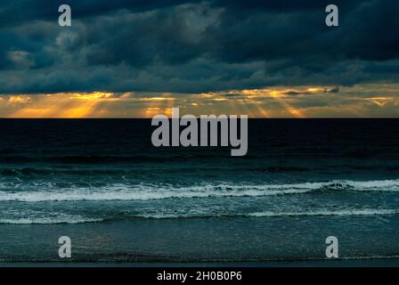 Sonnenstrahlen brechen durch dunkle Sturmwolken über dem Meer in Cardigan Bay, Wales, Großbritannien. Stockfoto