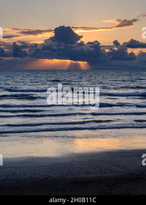 Sonnenstrahlen brechen durch den Daark Gewitterwolken über dem Meer in Cardigan Bay, Wales, Großbritannien. Stockfoto