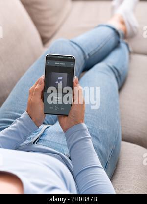 Frau, Die Musik Auf Dem Smartphone Anhörend, Während Sie Sich Auf Der Couch Zu Hause Entspannt Stockfoto