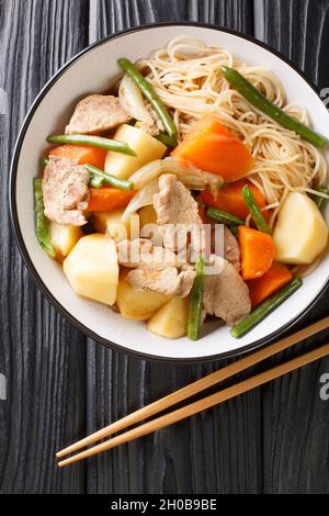 Nikujaga oder Fleisch und Kartoffeln ist ein leicht beruhigender japanischer Eintopf, der aus Schweinefleisch, Kartoffeln und Karotten in einer Schüssel auf schwarzem Hintergrund in vertikaler Form zubereitet wird Stockfoto