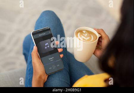 Schwarze Frau, Die Musik Auf Dem Smartphone Anhörend, Während Sie Sich Mit Kaffee Zu Hause Entspannt Stockfoto