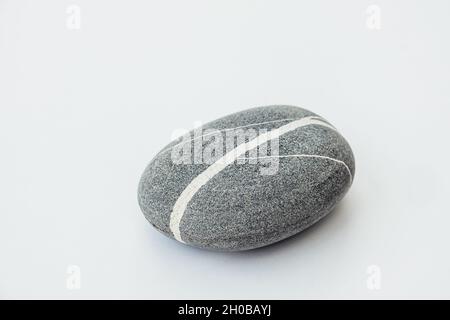 Ein Seestein in runder Form auf dem hellen Hintergrund. Draufsicht auf einen glatten Kieselstein. Stockfoto
