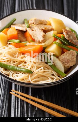 Nikujaga oder Fleisch und Kartoffeln ist ein leicht beruhigender japanischer Eintopf, der aus Schweinefleisch, Kartoffeln und Karotten in einer Schüssel auf dem Holztisch zubereitet wird. Vertikal Stockfoto