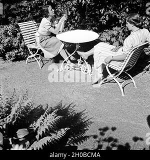 Zwei Frauen einer in der Prallen Sonne ein Einem Gartentisch, 1930er JAhre Deutschland. Zwei Frauen sitzen auf Gartenmöbel in der Sonne, Deutschland der 1930er Jahre. Stockfoto