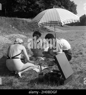 Ein Mann und zwei Frauen Artikel beim Picknick unter einem Sonnenschirm, Deutschland 1930er Jahre. Ein Mann und zwei Frauen in ein Pick Nick, während unter einem Sonnenschirm sitzen, Deutschland 1930, Stockfoto