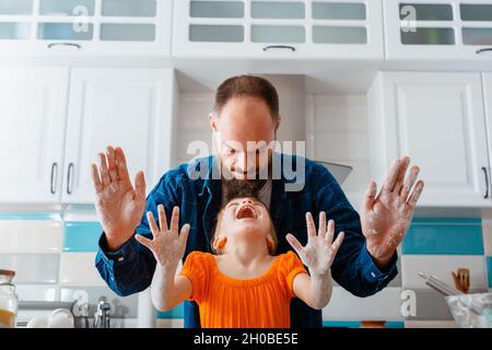 Kleines Mädchen haben Spaß spielen mit Papa beim Kochen Backen in der Küche. Tochter und kaukasischer Vater zeigen nach dem Teig die Hände schmutzig, lachen viel Spaß Stockfoto