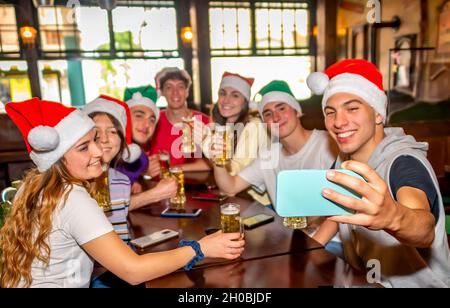 frohe weihnachten! Junge Gruppe von Teenagern, die ein Selfie-Portrait machen, um Weihnachten mit einem Weihnachtsmann-Hut in der Happy Hour in einem irischen Pub zu feiern Stockfoto