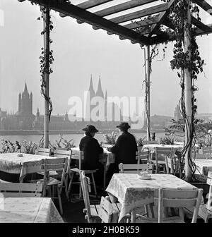 Zwei Damen sitzen in der Außenastronomie der Sünner Terrassen in Deutz und schauen auf die Skyline von Köln, Deutschland 1930er Jahre. Zwei Frauen genießen den Blick auf die Kölner Skyline von Deutz, Deutschland 1930er Jahre. Stockfoto