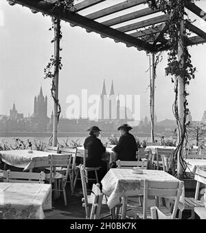 Zwei Damen sitzen in der Außenastronomie der Sünner Terrassen in Deutz und schauen auf die Skyline von Köln, Deutschland 1930er Jahre. Zwei Frauen genießen den Blick auf die Kölner Skyline von Deutz, Deutschland 1930er Jahre. Stockfoto