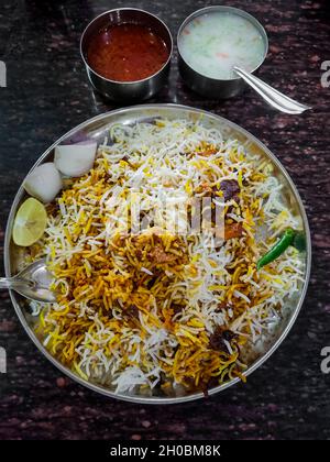 Hammelfleisch oder Lammbiriyani mit Basmati-Reis, serviert auf einem Teller mit Raita oder Joghurt-Dip und Gurke Stockfoto