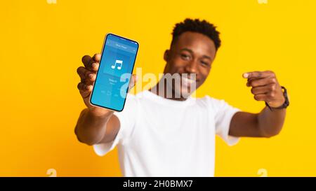 Aufgeregt Black Guy Zeigt Auf Smartphone Mit Musik-App-Schnittstelle Auf Dem Bildschirm Stockfoto