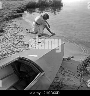 Eine junge Frau am Ufer eines Sieht mit einem KLEPPER Faltboot Typ T6 hält die Hände ins Wasser, Deutschland 1930. Eine junge Frau, die am Ufer eines Sees mit einem KLEPPER Faltboot hielt ihre Hände in das Wasser, Deutschland 1930. Stockfoto