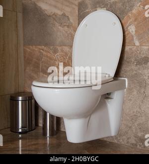 Toilette in der Toilette mit Mülleimer in der Ecke, braune Keramikfliesen. Toilette innen Stockfoto