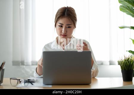 Asiatische Frau, die sich ein informatisches Webinar auf einem Laptop ansieht. Lächelnder junger Geschäftsmann, der Videoanruf mit den Partnern des Kunden führt Stockfoto