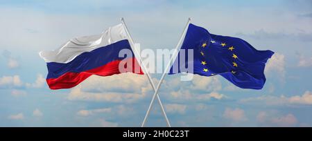 Die Flaggen Russlands und der Europäischen Union winken im Wind auf Fahnenmasten gegen den Himmel mit Wolken am sonnigen Tag. Symbolisieren Beziehung, Dialog zwischen Stockfoto