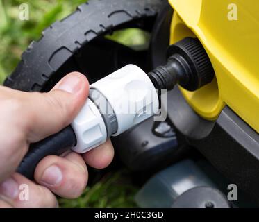 Mit der männlichen Hand wird die Schnellverschluss-Schlauchkupplung für Wasser aus nächster Nähe auf den Druckreiniger gesetzt. Industrie Stockfoto