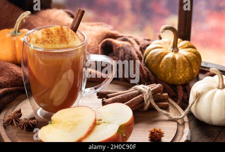 Tasse Apfelwein und Äpfel in Scheiben geschnitten auf einer Holzplatte mit Kürbissen an einem Fenster Stockfoto