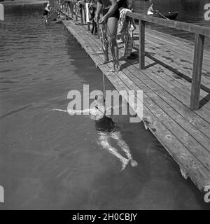 Der Bademeister hilft vom Holzsteg aus bei den ersten Schwimmversuchen in einem Badesee in Österreich, 1930er Jahre. Ein Bademeister helfen Schwimmen an einem See in Österreich, 1930er Jahre zu lernen. Stockfoto