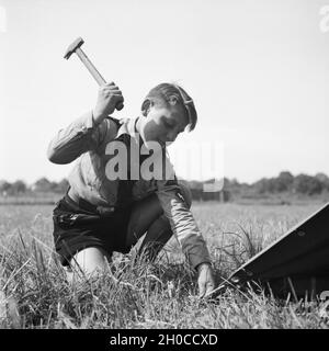 Ein Hitlerjunge schlägt einen Hering beim Zeltaufbau in die Erde von Westfalen, Deutschland 1930er Jahre. Ein Hitler Jugend Einrichten ein Zelt bei Westfalia, Deutschland 1930. Stockfoto