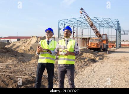 Zwei Ingenieure mit Helmen und Westen, die per Fernbedienung mit der Drohne arbeiten. Technologische Innovationen in der Bauindustrie Stockfoto