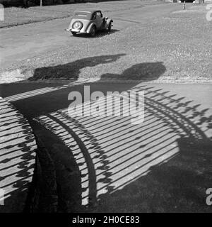 Ein Auto parkt in der Sonne, davor sterben Schatten des schmiedeeisernen Zaunes der Orangerie in Fulda, Deutschland 1930erJahre. Ein Parkplatz in der Sonne, vor der es die Schatten der schmiedeeisernen Zaun von Fulda Orangerie, Deutschland 1930. Stockfoto