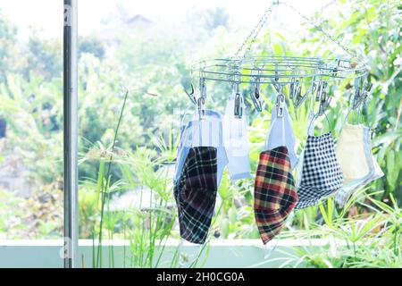 Bunte Gesichtsmasken aus Stoffen hängen mit Wäscheklammer. Verschwommenes Grün hinterlässt den Hintergrund. Speicherplatz kopieren. Stockfoto