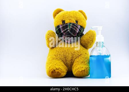 Der braune Teddybär trägt eine Maske und daneben eine blaue Desinfektionsgel-Flasche. Weißer Hintergrund, Kopierbereich. Stockfoto