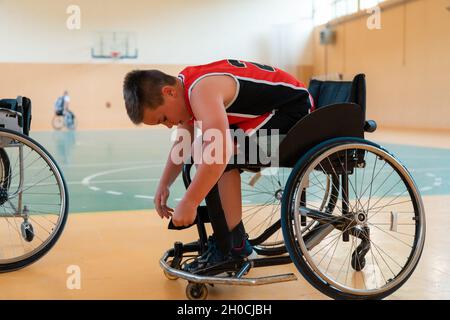 Der Junge sitzt im Rollstuhl und bereitet sich auf den Basketballstart in der großen Arena vor Stockfoto