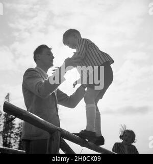 Ein Mann Hält Einen Kleinen Jungen, der Auf Einem Burgrestaurant Balanciert, 1930er Jahre Deutschland. Ein Mann hält einen kleinen Jungen, auf einem Geländer, Deutschland der 1930er Jahre balanciert.