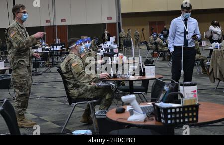 Personal Sgt. Matthew Tybor vom 108. Multifunktionalen medizinischen Bataillon der Illinois Army National Guard weist jemanden am 25. Januar an einen Tisch im Tinley Park Convention Center, einer Massenzunmpfungsstelle für COVID-19 in Tinley Park, Illinois. Tybor, der in Tinley Park lebt, sagte, dass die Arbeit am Standort für ihn von großer Bedeutung ist, besonders da er seinen Vater Terrence am 28. November an COVID-19 verloren hat. „Es ist sowohl fantastisch als auch surreal“, sagte er. „Ich freue mich sehr, auf dieser Mission zu sein und dabei zu helfen, diese Pandemie zu beenden.“ Stockfoto