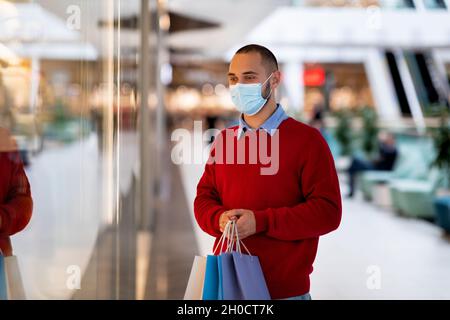 Einkaufen während des covid Pandemiekonzepts. Junger kaukasischer Kerl in Gesichtsmaske hält Einkaufstaschen im Supermarkt Stockfoto