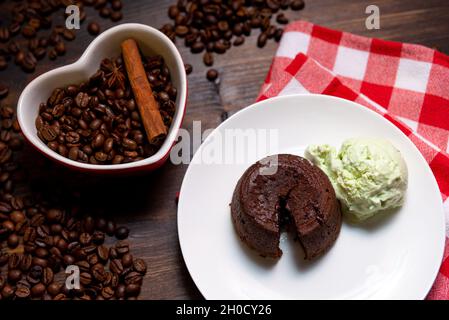 Eine Portion Schokoladenfondant mit einer Kugel Pistazien-Eis auf einem Teller. Im Hintergrund befindet sich eine herzförmige Tasse, gefüllt mit Kaffeebohnen und einem Stockfoto