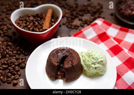 Eine Portion Schokoladenfondant mit einer Kugel Pistazien-Eis auf einem Teller. Im Hintergrund befindet sich eine herzförmige Tasse, gefüllt mit Kaffeebohnen und einem Stockfoto