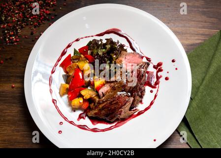 Chateaubriand von zartem Rindfleisch in Bordeaux-Weinsauce mit Gemüsesauce. Großer Teller mit Speisen auf einem dunkelbraunen Holzhintergrund. Stockfoto