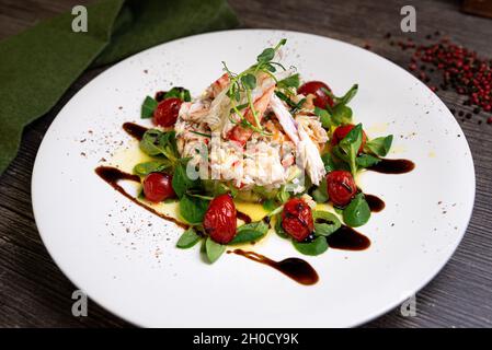 Salat mit Krabben, Gurken, Cocktailgarnelen, Avocado-Tatar und Mangosauce. Großer Teller mit Lebensmitteln. Salat mit Olivenöl, Balsamico-Sauce beträufelt. Stockfoto