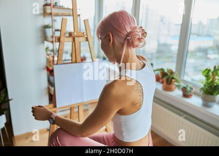 Elegante Künstlerin sitzt an der Staffelei mit weißer Leinwand auf zu Hause Stockfoto