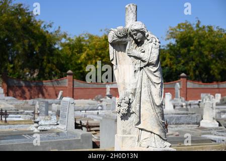 Skulptur einer Frau, die an einem sonnigen Tag auf einem Friedhof am Kreuz trauert Stockfoto