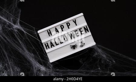 Whiteboard für Text mit dem Wort Happy Halloween, Fledermäuse und Spinnen im Spinnennetz auf schwarzem Hintergrund, Draufsicht, flach liegend. Konzeptkarte für den Stockfoto