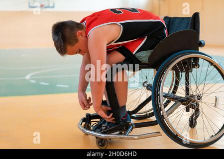 Der Junge sitzt im Rollstuhl und bereitet sich auf den Basketballstart in der großen Arena vor Stockfoto