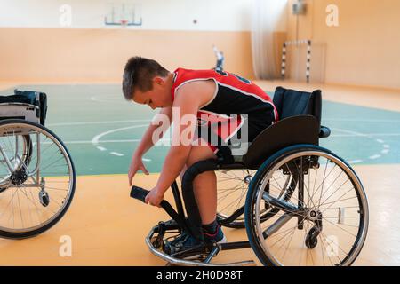 Der Junge sitzt im Rollstuhl und bereitet sich auf den Basketballstart in der großen Arena vor Stockfoto