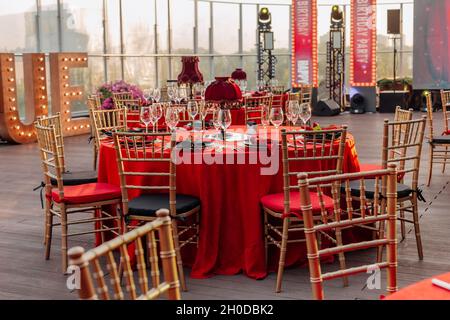 Tische und Stühle für Bankette in Schwarz, Rot und Gold. Eleganter Veranstaltungssaal: Dekor, Tischdecke, Teller, Servietten, Rosen, Brille Stockfoto