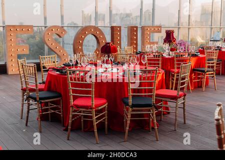 Tische und Stühle für Bankette in Schwarz, Rot und Gold. Eleganter Veranstaltungssaal: Dekor, Tischdecke, Teller, Servietten, Rosen, Brille Stockfoto