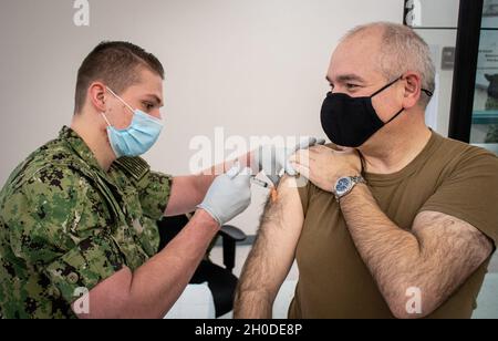 210201-N-RG482-0014 SILVERDALE, Washington (Feb 1, 2021) - der Hospitalist Logan Parker (links), ein Mitarbeiter im Gesundheitswesen, der dem Navy Medicine Readiness and Training Command Bremerton zugewiesen wurde, verabreicht die erste Dosis des COVID-19-Impfstoffes an den Navy Capt. Jon Moretty, den Kommandanten des Naval Undersea Warfare Center Division Keyport, im Bangor Health Education Center. Der Impfstoff wird für Mitarbeiter im Gesundheitsbereich vor Ort, zusammen mit anderen Ersthelfern, einschließlich des Personals des medizinischen Notdienstes, der Sicherheitskräfte und anderen wichtigen Mitarbeitern, bereitgestellt, gefolgt von Gesundheits- und Supportmitarbeitern in Mi Stockfoto