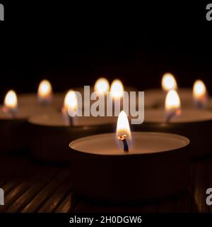 Gruppe von Teelichterkerzen, die mit weichen, warmen Flammen in einer dunklen Umgebung brennen Stockfoto