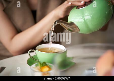 asiatische Frau, die am Tisch sitzt und eine Teetaße mit Tee füllt Stockfoto