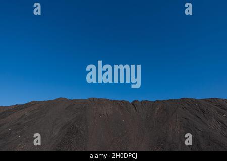 Ein Haufen von Mineralstoffen in Kohlekraftwerken. Das an einem sonnigen Tag aufgenommene Foto kontrastiert das Schwarz der Kohle mit dem Blau des Himmels. Stockfoto